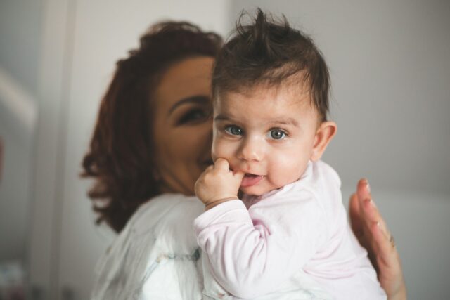 Een vrouw houdt een baby op haar arm, de baby kijkt in de camera