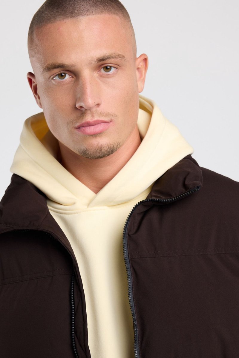 Bodywarmer Jai in donkerbruin met hoge kraag en grove rits, gedragen over een hoodie